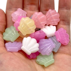May include: A handful of translucent seashell beads in various pastel colors, including pink, yellow, green, and purple. The beads are small and have a glossy finish, perfect for jewelry making or craft projects.