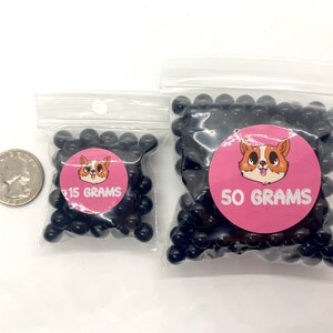 May include: Two bags of black beads, one bag labeled "15 GRAMS" and the other labeled "50 GRAMS". Both bags feature a cartoon dog with pink ears and a pink background.