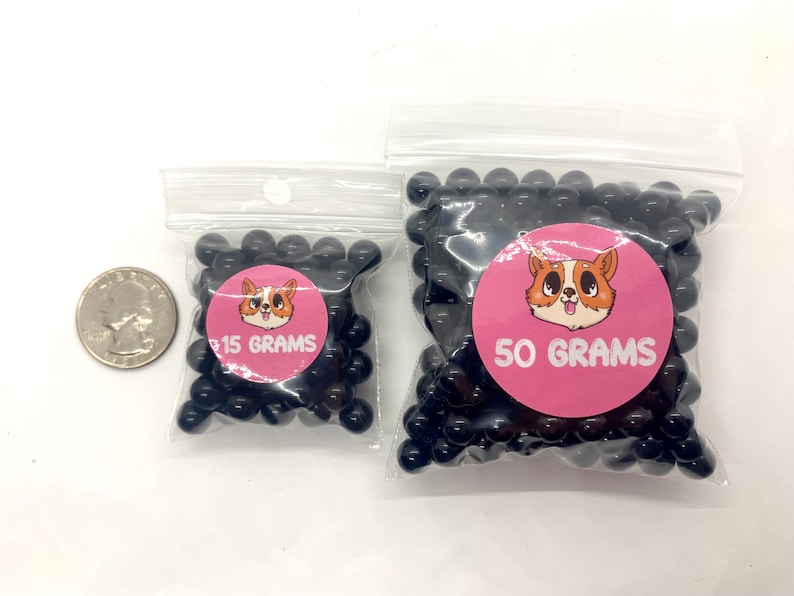 May include: Two bags of black beads, one bag labeled "15 GRAMS" and the other labeled "50 GRAMS". Both bags feature a cartoon dog with pink ears and a pink background.