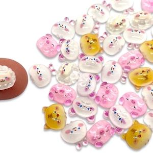 May include: A collection of small, colorful, animal-shaped resin embellishments. The assortment includes pig, sheep, and bear designs in pink, white, and yellow. The embellishments are small, with the largest being about 0.5 inches.