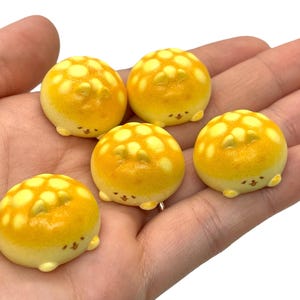 May include: Five yellow and white mini ceramic sculptures shaped like buns with cute faces. The buns have a honeycomb pattern.
