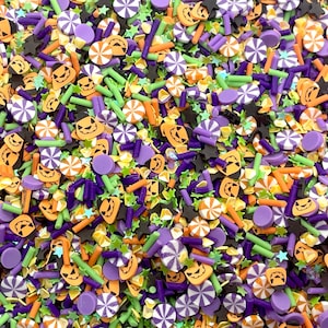 May include: A variety of Halloween sprinkles in orange, green, purple, and black. The sprinkles include jack-o'-lantern faces, stars, candy canes, and small sticks.