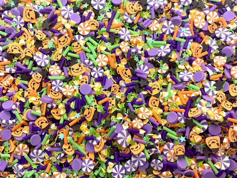 May include: A variety of Halloween sprinkles in orange, green, purple, and black. The sprinkles include jack-o'-lantern faces, stars, candy canes, and small sticks.