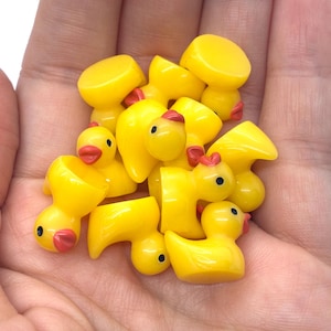 May include: A collection of small, bright yellow plastic duck figurines. Each duck features a smooth, rounded body, a distinct orange beak, and a single black dot for an eye. The ducks are molded in a uniform shape, appearing as miniature replicas.
