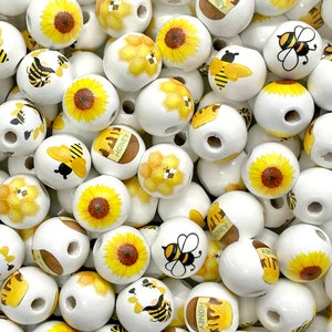 May include: A collection of white wooden beads with various bee and sunflower designs. The beads have a hole through the center for stringing.