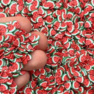 May include: A close-up of a pile of red and green watermelon slice shaped confetti. The confetti is made of a soft, pliable material and is perfect for adding a fun and festive touch to crafts and decorations.
