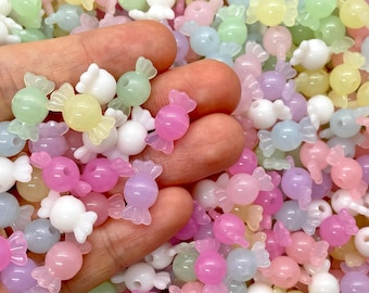 Puede incluir: Un puñado de cuentas en forma de caramelo de colores pastel en tonos rosa, morado, amarillo, verde y blanco. Las cuentas son pequeñas y translúcidas, con un diseño de caramelo envuelto. Ideal para bisutería o manualidades.