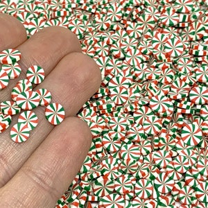 May include: A close-up of a hand holding a pile of small, round, candy cane-shaped, red and green sprinkles. The sprinkles are perfect for decorating cakes, cupcakes, and other desserts.