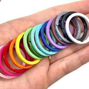 May include: A set of 15 colorful key rings in various shades of pink, red, orange, yellow, green, blue, purple, and grey. The key rings are made of metal and have a smooth finish.