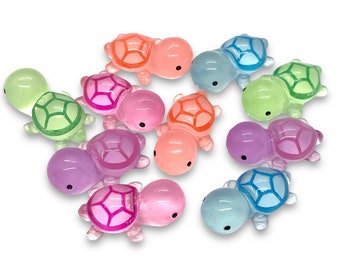 May include: A collection of ten small, colorful turtle figurines. The turtles are made of plastic and have a glossy finish. They are all different colors, including pink, purple, green, blue, and orange.