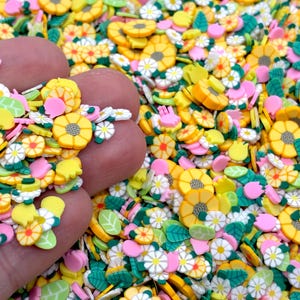 May include: A collection of small, flat, circular polymer clay slices featuring floral and botanical designs. The assortment includes yellow sunflowers, white daisies, pink tulips, and green leaves, all rendered in vibrant, solid colors.