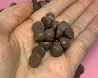 May include: A collection of brown, round, and pointed plastic embellishments. The embellishments are in a hand, and they appear to be for crafting or jewelry making.