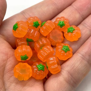 May include: A handful of small, orange pumpkin-shaped beads with green stems. These translucent beads are a vibrant orange color and are perfect for crafting projects or seasonal decorations. The beads are small, measuring approximately 0.5 inches in diameter.