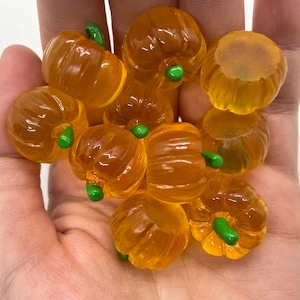 May include: A collection of orange and green pumpkin-shaped candies. The candies are arranged in a hand, with the stems facing up.