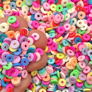 May include: A large pile of colorful plastic donut-shaped beads. The beads are in various shades of pink, blue, green, yellow, orange, and red.