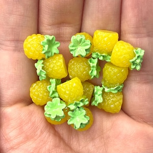 May include: A collection of yellow and green pineapple shaped resin charms. The charms are small and perfect for adding a tropical touch to crafts.