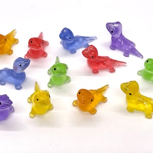 May include: A collection of ten small, colorful, plastic lizard figurines. The lizards are in various poses and are made of translucent plastic. The colors include red, orange, yellow, green, blue, and purple.