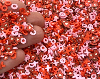 May include: A close-up of a pile of red, pink, and brown sprinkles shaped like hearts, circles, and the letters "x" and "o".