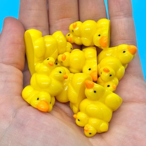 May include: A handful of small, yellow duck figurines with orange beaks and black eyes. The ducks are clustered together, creating a playful and cheerful scene. The background is a solid light blue.