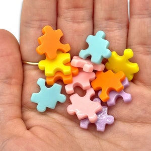 May include: A pile of colorful puzzle pieces in various pastel shades, including light blue, pink, yellow, and orange. The pieces are made of plastic and have a smooth, glossy finish.