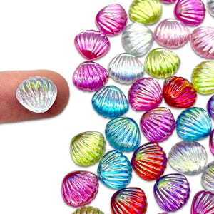 May include: A collection of colorful, iridescent seashell-shaped beads in various colors, including pink, blue, green, and red. One bead is held by a finger, showcasing its translucent quality. These beads are ideal for crafting and jewelry making.