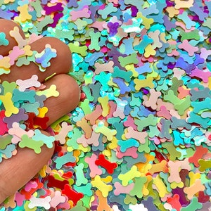 May include: A large pile of iridescent bone-shaped glitter in various pastel colors, including pink, blue, green, and yellow.