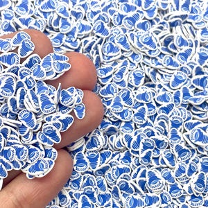 May include: A large quantity of blue and white shell-shaped sprinkles. The sprinkles are small and have a white outline with a blue center.