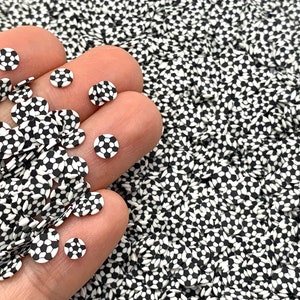 May include: A close-up of a hand holding a pile of black and white soccer ball patterned sprinkles. The sprinkles are small and round, and they are perfect for decorating cakes, cupcakes, and other desserts.