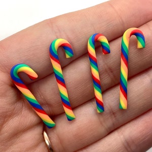May include: Four rainbow candy cane charms made of polymer clay. The candy canes are red, orange, yellow, green, blue, and pink.