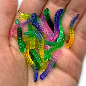 May include: A collection of colorful, translucent plastic worm-shaped fishing lures in shades of green, yellow, pink, and blue.
