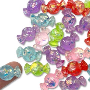 May include: Assortment of colorful candy-shaped resin embellishments with iridescent glitter. The candy shapes are in various colors, including blue, green, purple, pink, and red.