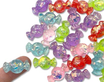May include: Assortment of colorful candy-shaped resin embellishments with iridescent glitter. The candy shapes are in various colors, including blue, green, purple, pink, and red.