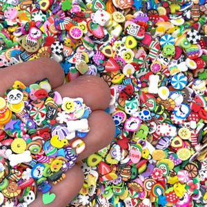 May include: A handful of colorful polymer clay embellishments in various shapes, including fruits, animals, and sweets. The assortment features a panda, a strawberry, a slice of orange, and a smiley face. The background is filled with similar miniature decorations.
