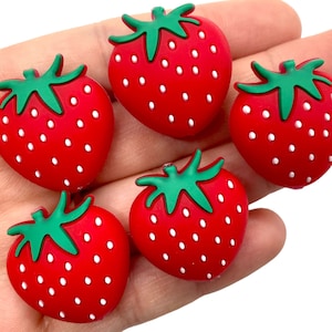 May include: Five red silicone strawberry charms with green leaves and white seeds.