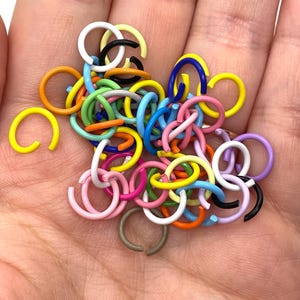 May include: A collection of colorful metal jump rings in various sizes and colors, including yellow, orange, red, pink, purple, blue, green, and black.