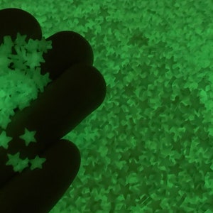 May include: A close-up of a hand holding a pile of green glow-in-the-dark star-shaped confetti.
