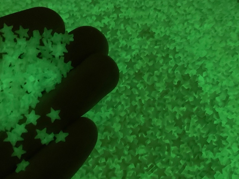 May include: A close-up of a hand holding a pile of green glow-in-the-dark star-shaped confetti.