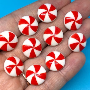 May include: A collection of nine small, round, flat buttons featuring a classic red and white peppermint swirl pattern. Each button has a smooth, glossy finish with a radial design radiating from the center, resembling a traditional hard candy.