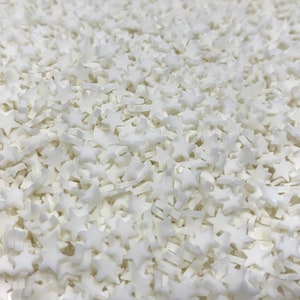 May include: A close-up image of a large quantity of white star-shaped sprinkles. The sprinkles are small and perfect for decorating cakes, cupcakes, and other desserts.
