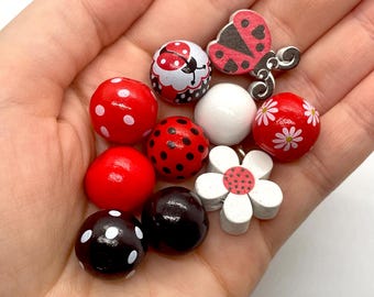 May include: A collection of wooden beads with ladybug and flower designs. The beads are red, black, white, and pink with black and white polka dots.