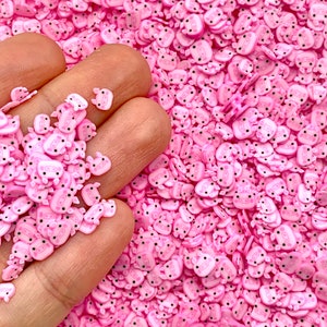 May include: Pink and white pig-shaped sprinkles. The sprinkles are small and have a glossy finish.