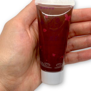 May include: A brown tube of lip gloss with a white cap. The tube has a pink butterfly design and the words "Love" and "Beauty" in pink.