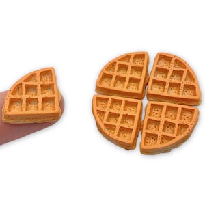 May include: Four pieces of miniature waffle cookies, each with a light brown color and a waffle pattern. One piece is held by a finger.