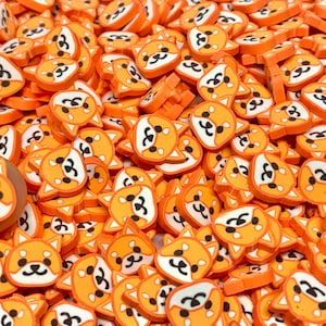 May include: A large quantity of small, orange and white resin charms shaped like cartoon Shiba Inu dogs. The charms have black eyes and noses and are perfect for adding a cute touch to crafts and jewelry.
