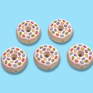 May include: Five donuts with pink frosting and colorful candy sprinkles are arranged on a light blue background. Each donut has a hole in the center and a light brown base. The sprinkles are various colors.
