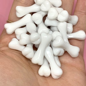May include: A pile of white plastic bone-shaped charms. The charms are small and have a glossy finish.
