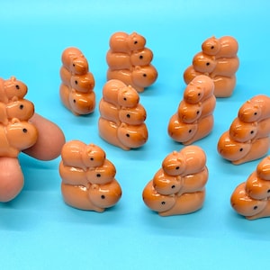 May include: A collection of small, orange capybara figurines. Each figurine is stacked with multiple capybaras, creating a unique and playful design. The figurines are set against a bright blue background.