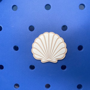 May include: A blue plastic tote bag with a white seashell charm. The bag has a textured surface with small holes.