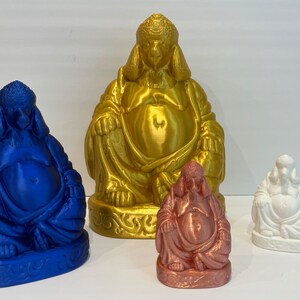 May include: Four Buddha statues in varying sizes and colors. The largest is gold, the next is blue, followed by a copper-colored statue, and the smallest is white. All statues are seated with a serene expression and detailed robes.