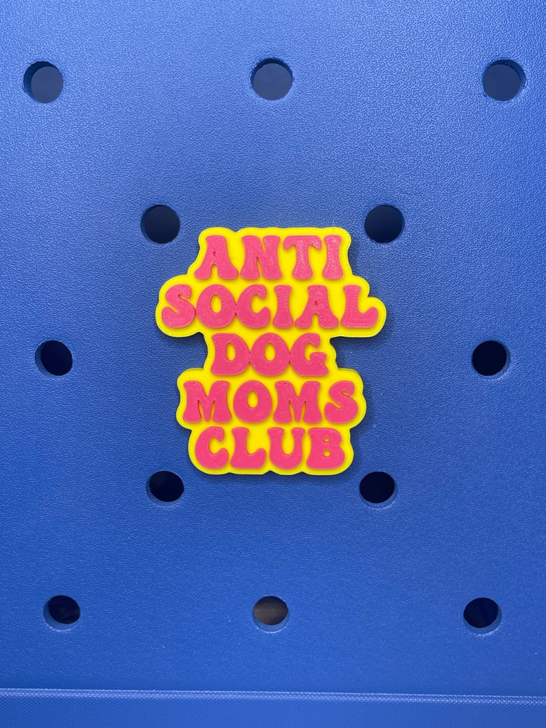 May include: A yellow and pink 3D sticker with the text "Anti Social Dog Moms Club" in a retro font.